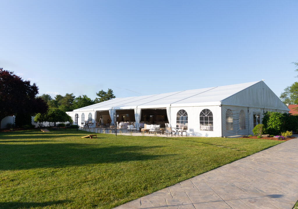 A stunning image of a wedding ceremony at The Villa in Bridgewater, capturing the elegant outdoor setting with manicured gardens and a charming gazebo. The soft, natural light creates a romantic ambiance as the couple exchanges vows, with guests seated on the beautifully arranged lawn. The venue’s classic architecture and picturesque surroundings make it a truly enchanting backdrop for a memorable day.