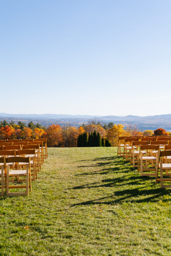 A picturesque photo of a wedding ceremony at Steele Hill Resort in Sanborton, with the couple exchanging vows against the breathtaking backdrop of New Hampshire’s lakes and mountains. The expansive views of the rolling hills and sparkling water create a serene and dramatic atmosphere, while the soft, natural light adds a romantic touch. The resort’s stunning outdoor setting provides the perfect combination of nature’s beauty and elegant celebration.