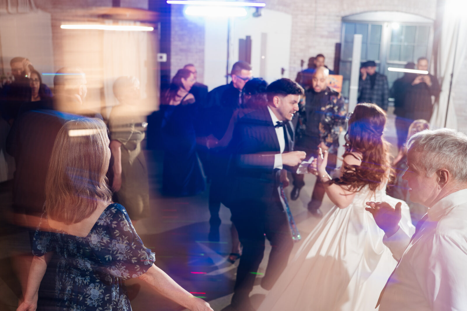 Wedding reception dance floor with guests dancing, including friends in blow-up suits, celebrating to Bad Bunny’s music.