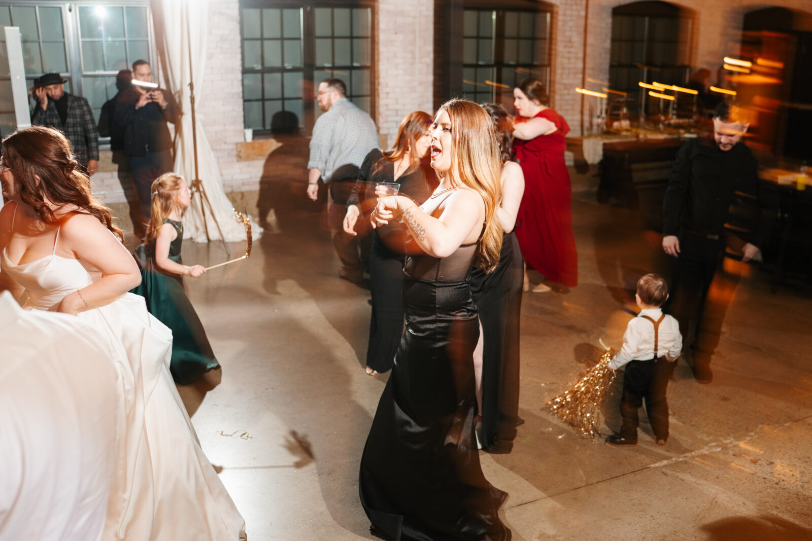 Wedding reception dance floor with guests dancing, including friends in blow-up suits, celebrating to Bad Bunny’s music.