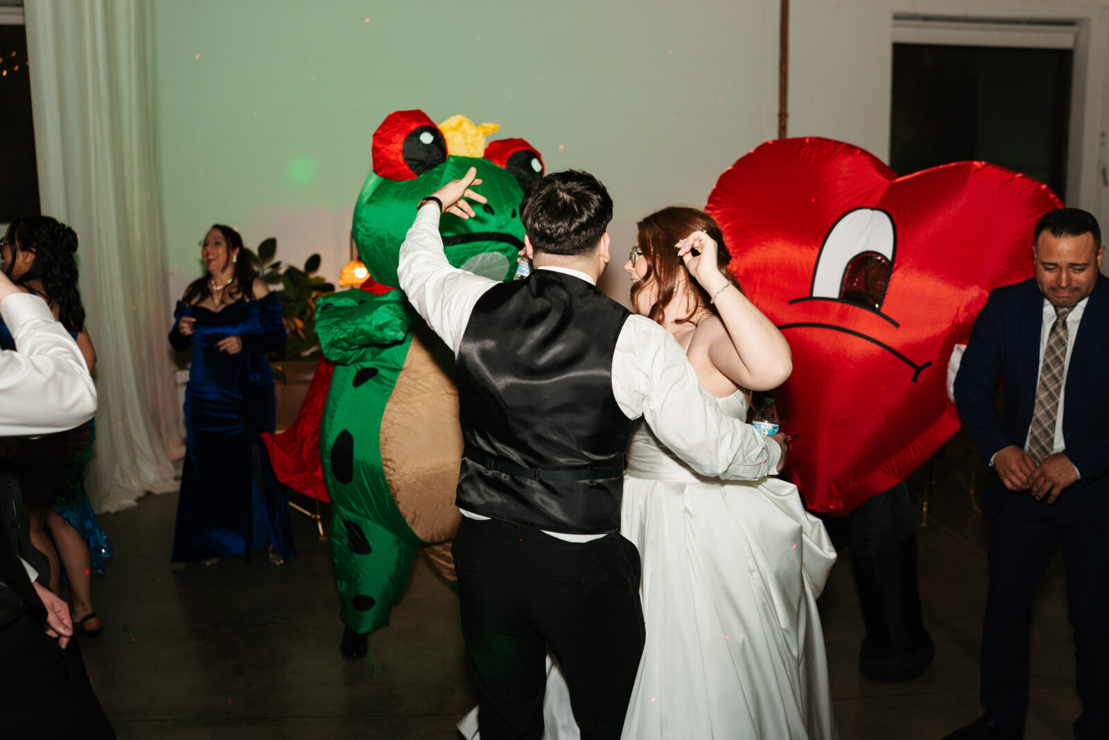 Wedding reception dance floor with guests dancing, including friends in blow-up suits, celebrating to Bad Bunny’s music.