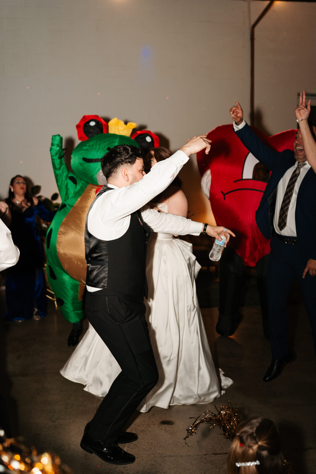 Wedding reception dance floor with guests dancing, including friends in blow-up suits, celebrating to Bad Bunny’s music.