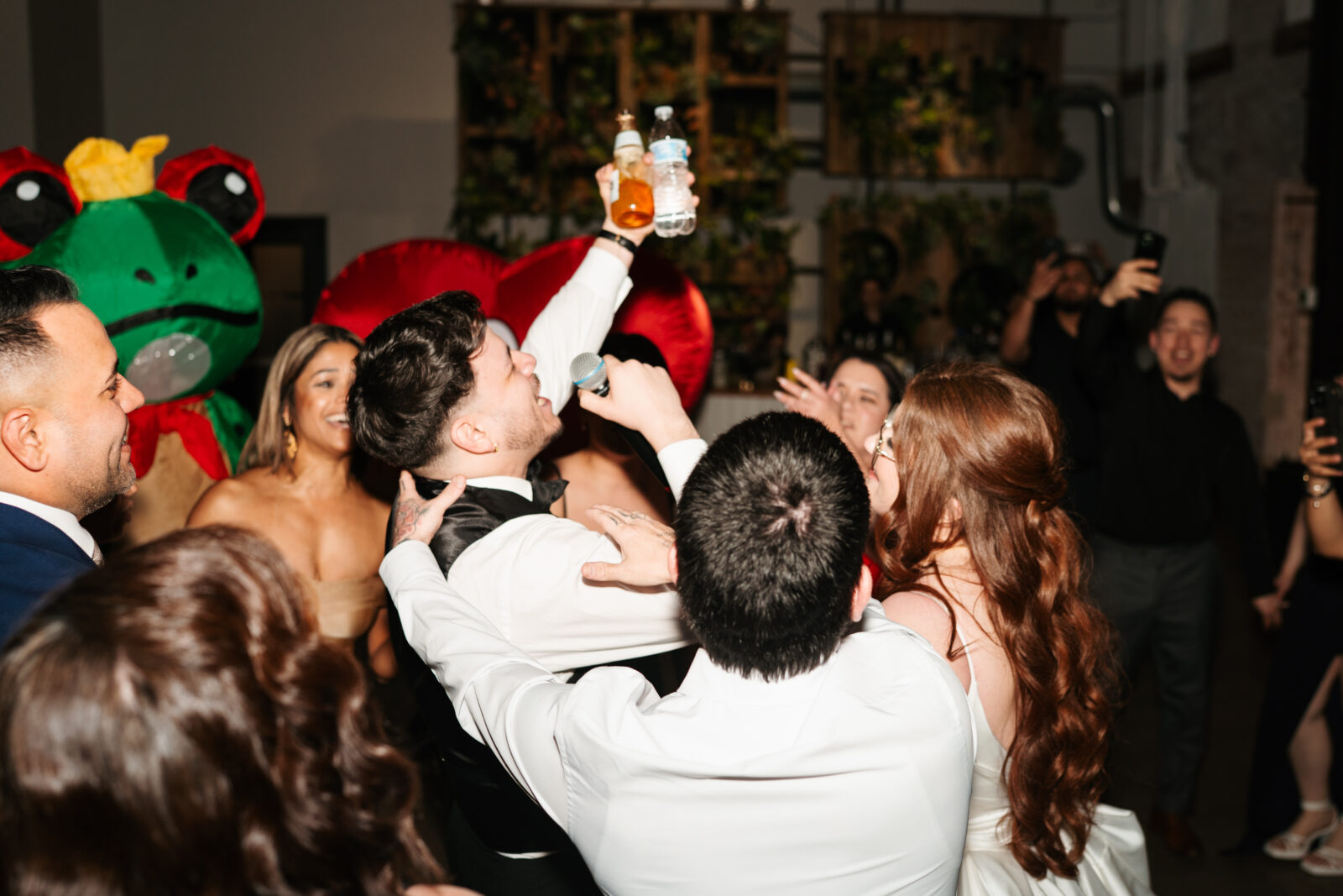 Wedding reception dance floor with guests dancing, including friends in blow-up suits, celebrating to Bad Bunny’s music.