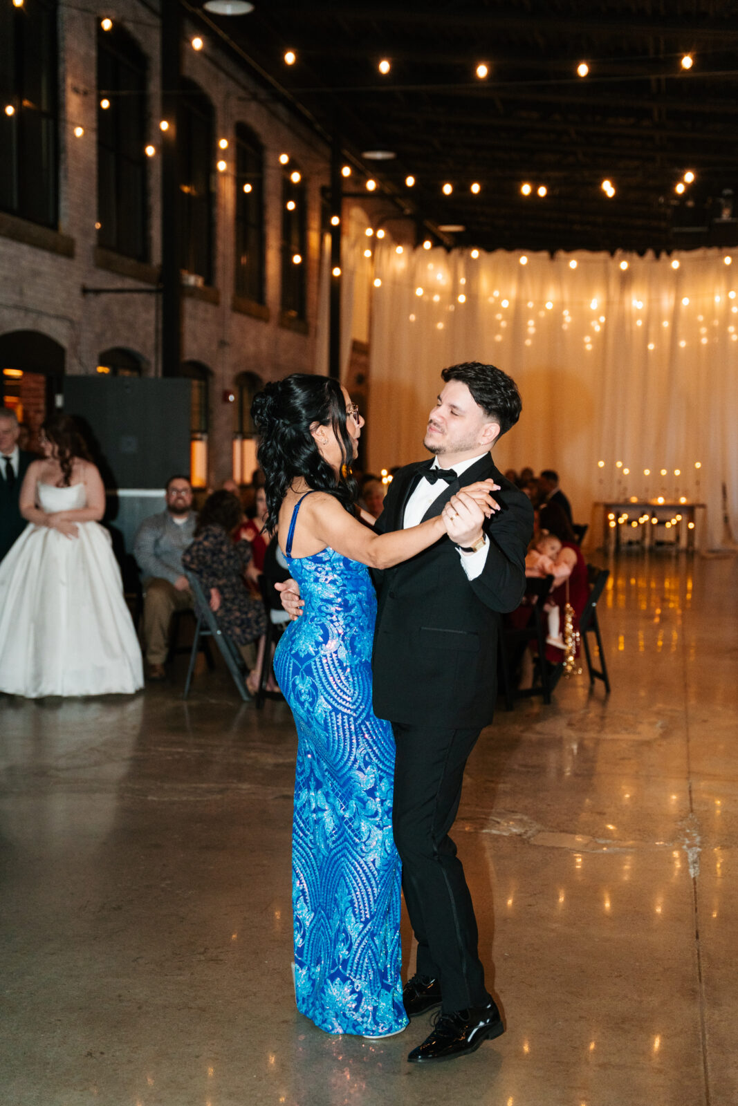 Wedding reception dance floor with guests dancing, including friends in blow-up suits, celebrating to Bad Bunny’s music.