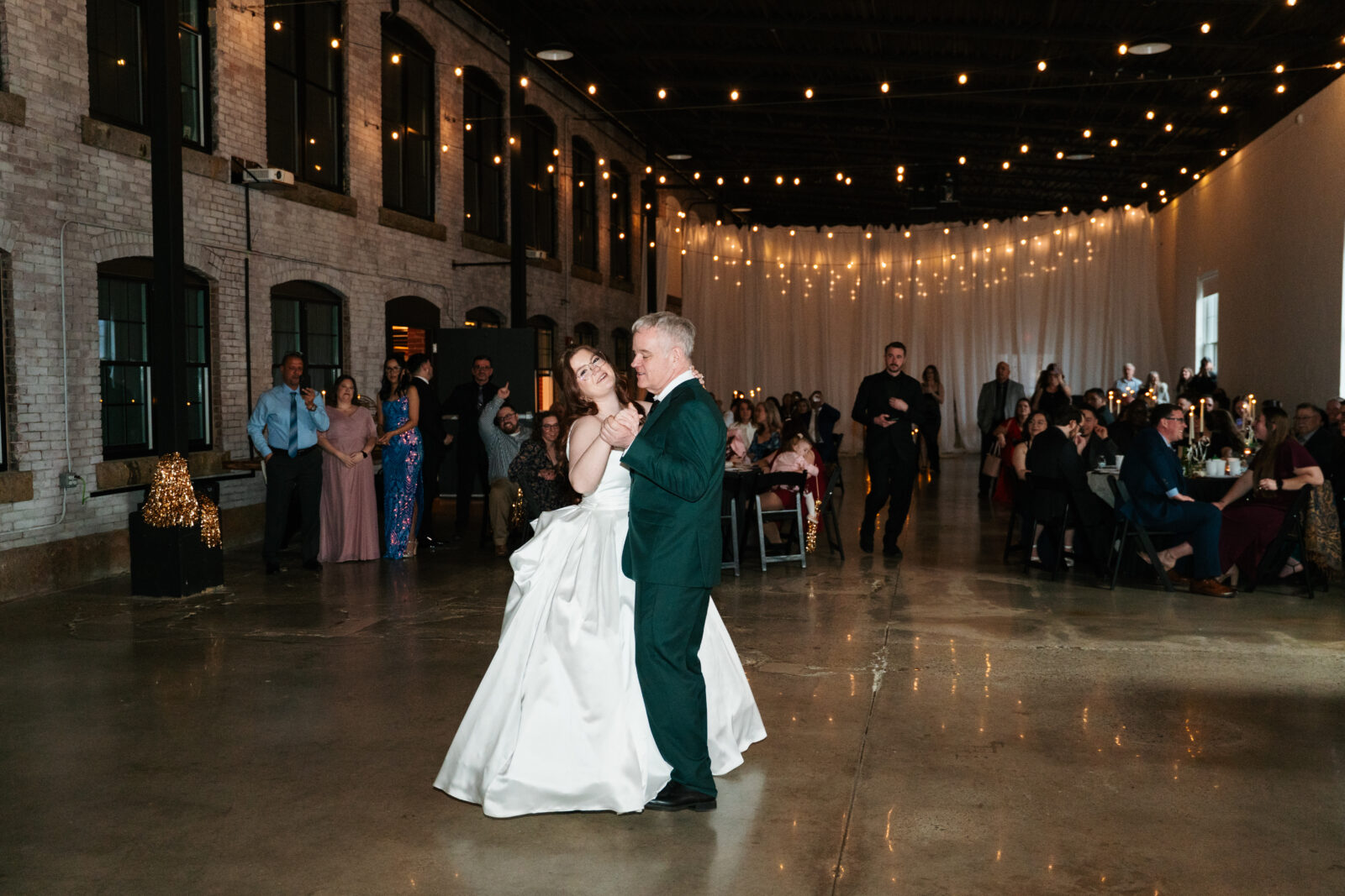 Wedding reception dance floor with guests dancing, including friends in blow-up suits, celebrating to Bad Bunny’s music.