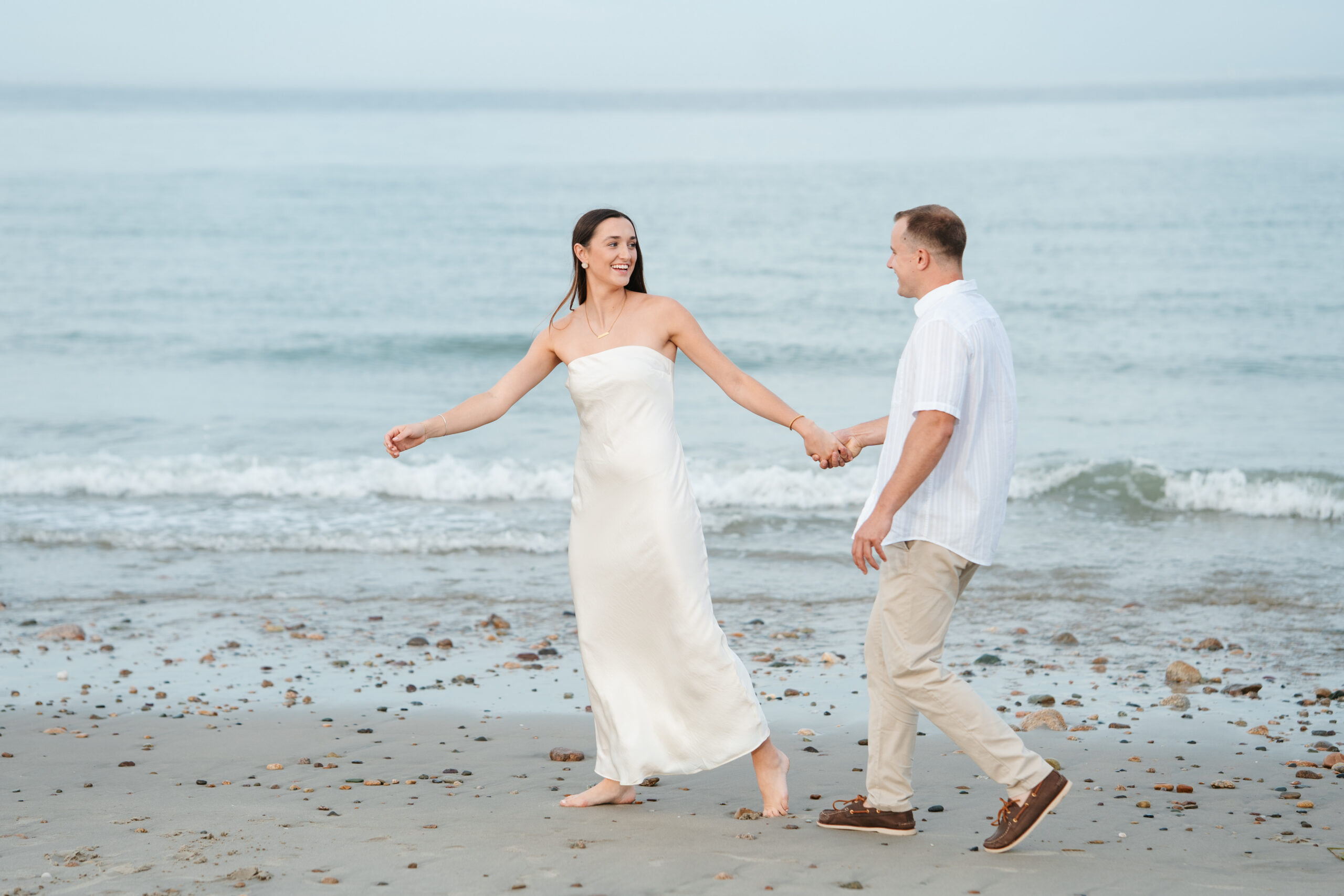 Couple walking barefoot along the shoreline during their beach engagement session.
