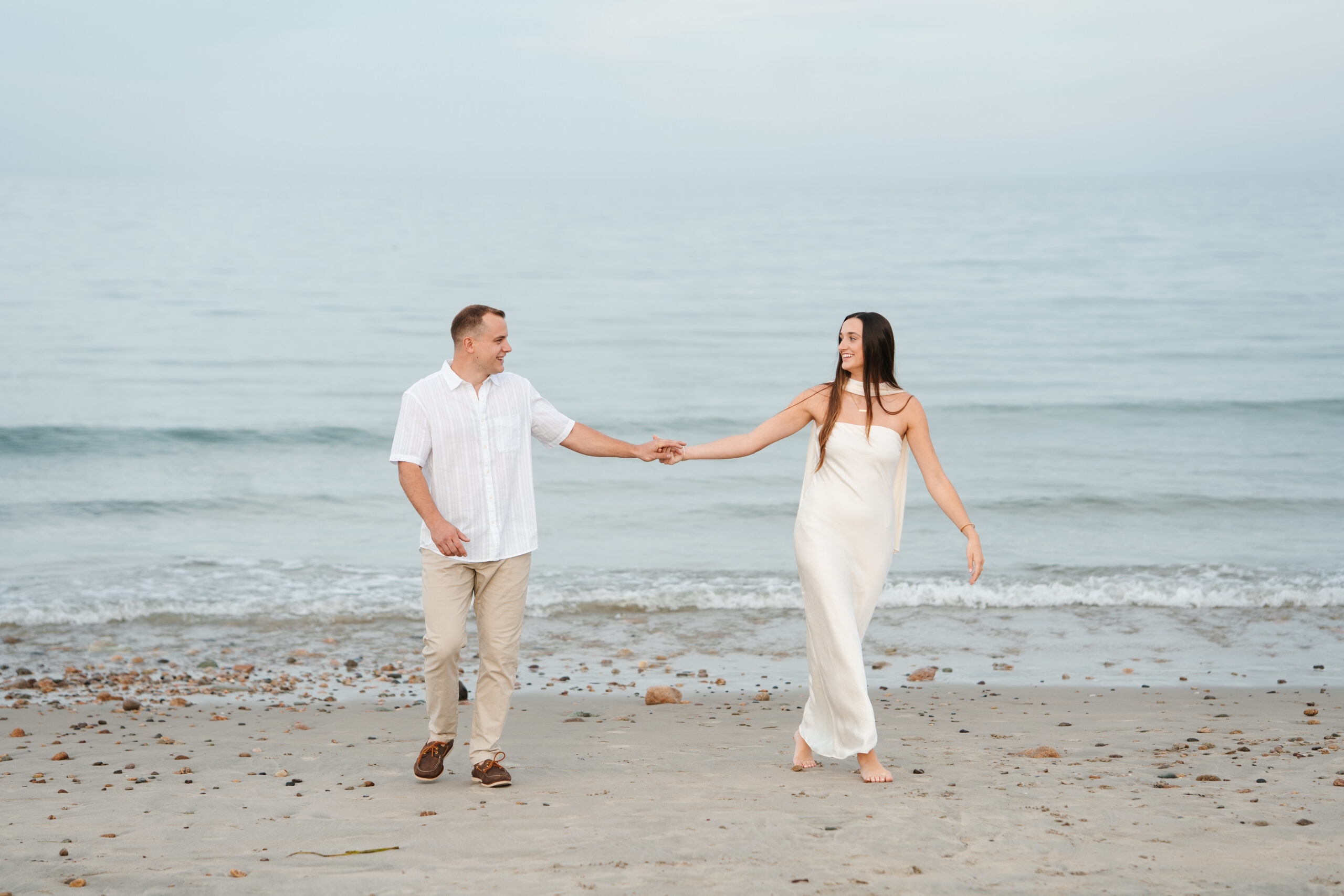 Wind-swept hair and candid laughter during a coastal engagement photo session.