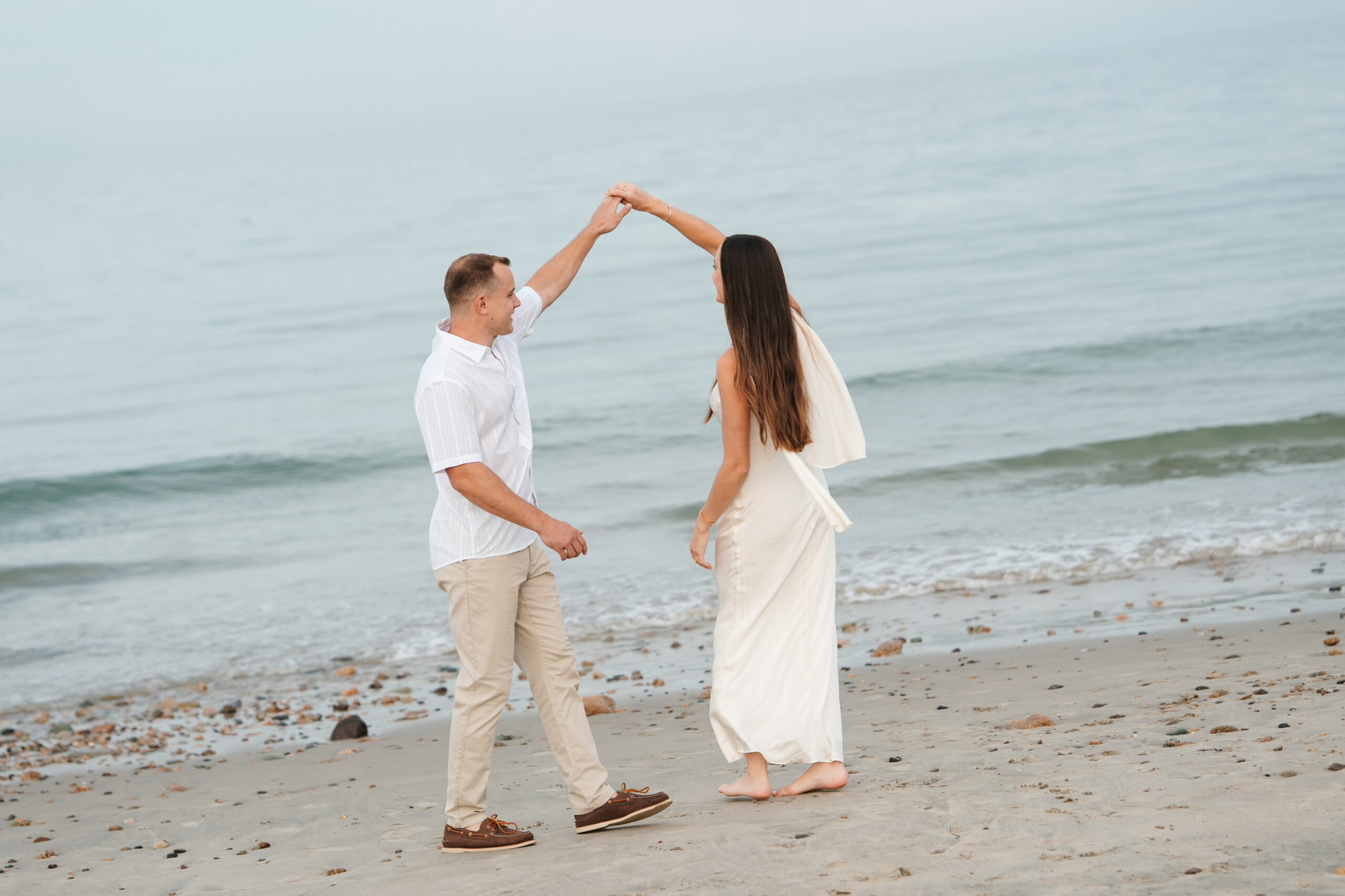 Engaged couple laughing together on a quiet coastal beach at golden hour.